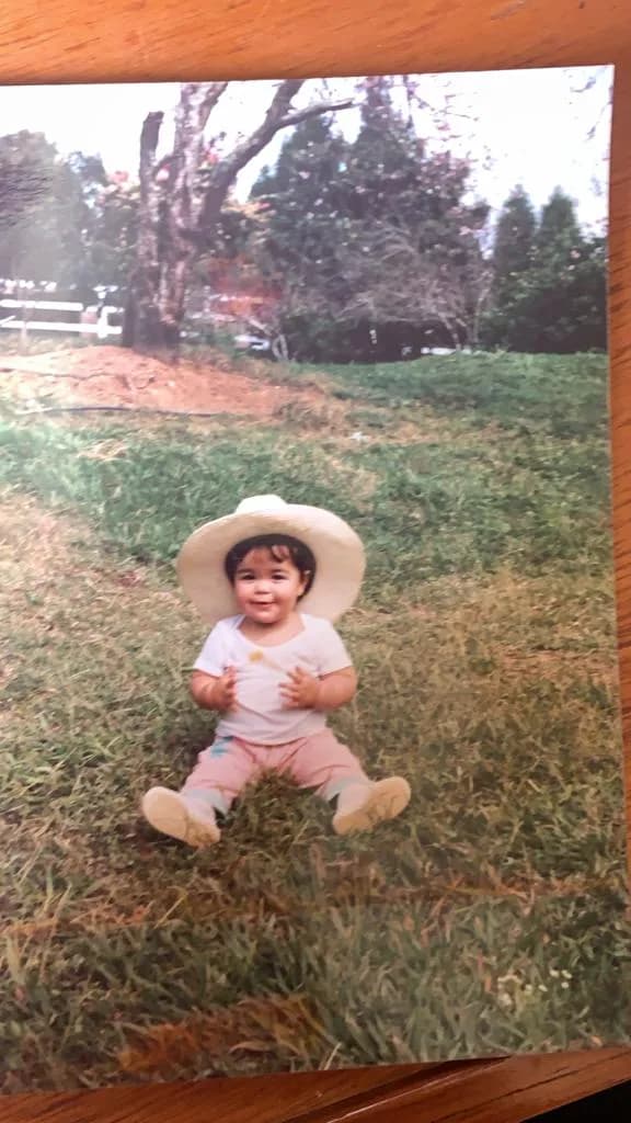 Júlia as a toddler in a straw hat, sitting on the grass
